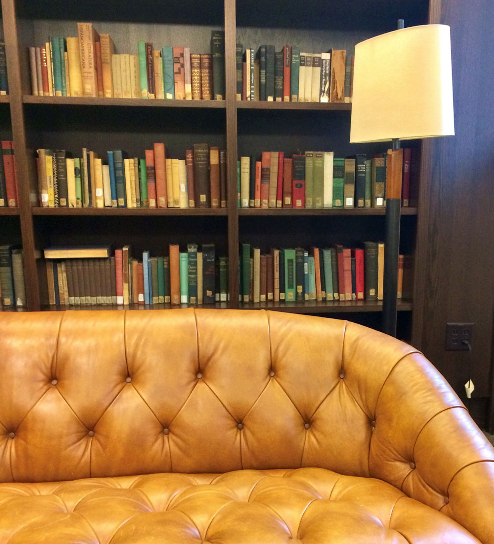 Couch with bookcase filled with books in library warm space for reading.